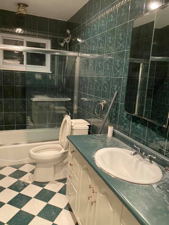 Green-tiled bathroom with checkered floor, bathtub, toilet, sink, and mirrored vanity