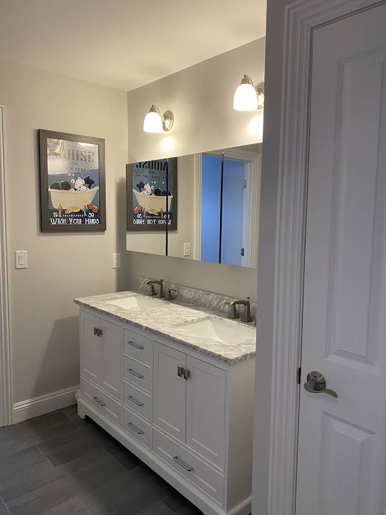 White bathroom vanity with marble countertop, double mirrors, and wall sconces in a gray room.