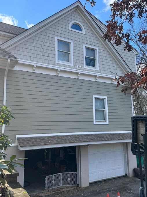 Two-story gray house with white trim, garage door, and front awning under a blue sky