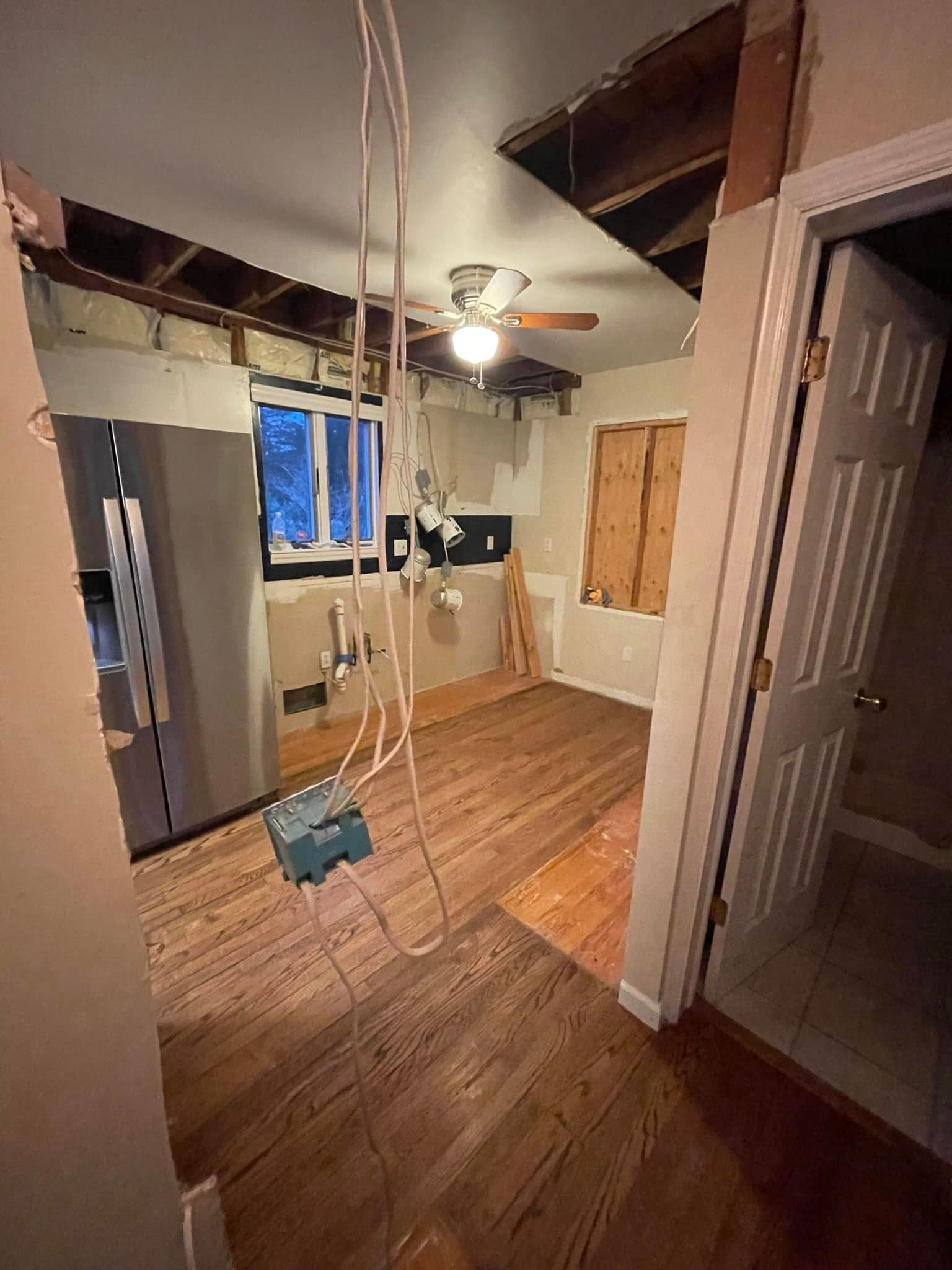 Partially renovated room with exposed beams, hanging wires, ceiling fan, and hardwood floor