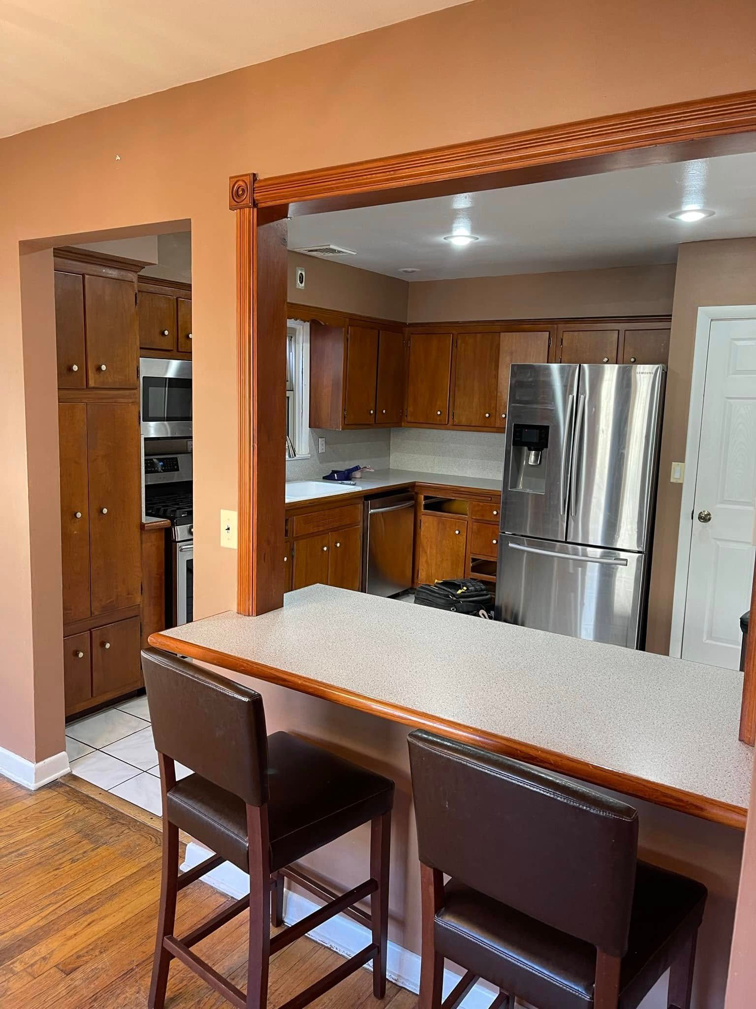 Open kitchen with stainless steel appliances, wood cabinets, and a breakfast bar with two stools Open kitchen with stainless steel appliances, wood cabinets, and a breakfast bar with two stools