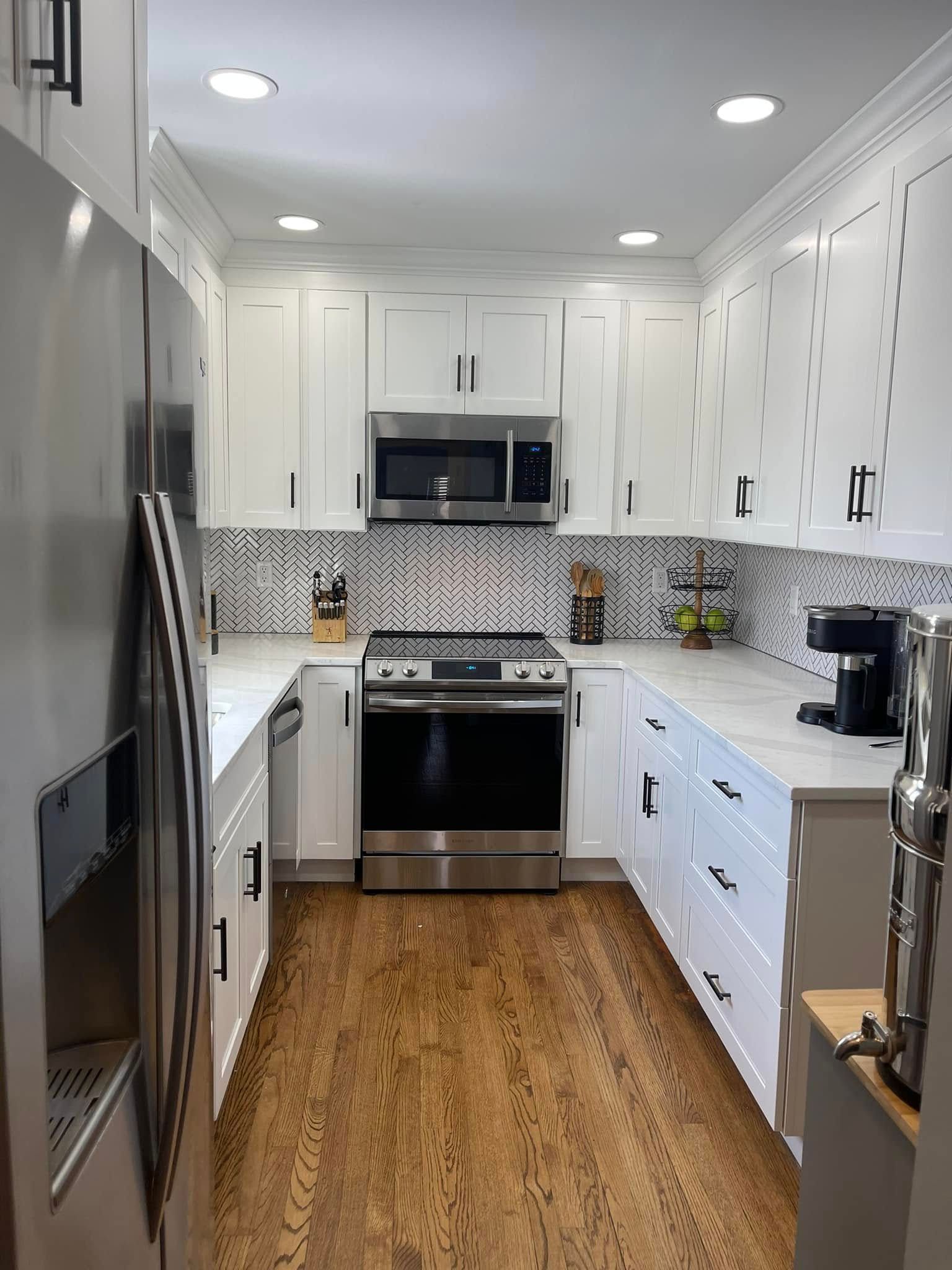 Bright white galley kitchen with stainless steel appliances, wood floor, and black-and-white patterned backsplash