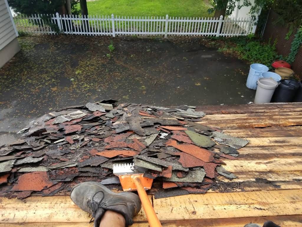 Roof shingles piled on a roof during repair, with a driveway and fence in the background