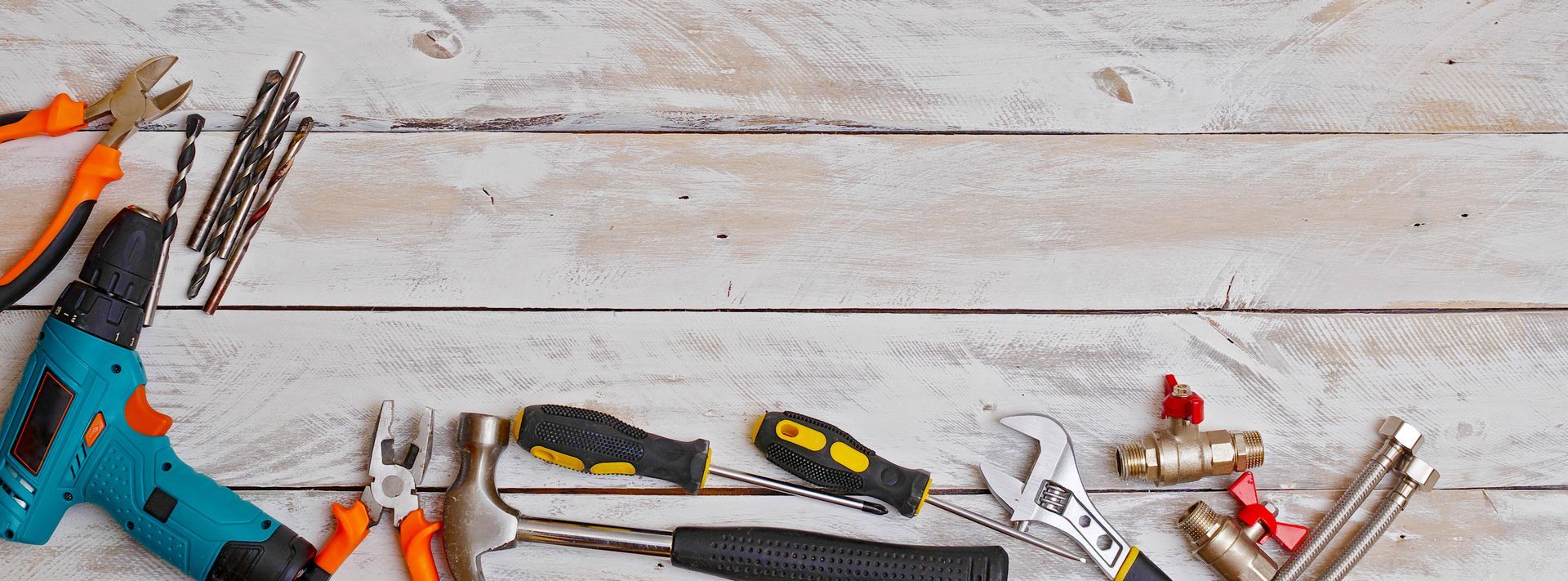 Handyman tools including a drill, hammer, pliers, and wrench arranged on a white wood surface, representing general handyman services in Ridgewood, NJ Handyman tools including a drill, hammer, pliers, and wrench arranged on a white wood surface, representing general handyman services in Ridgewood, NJ