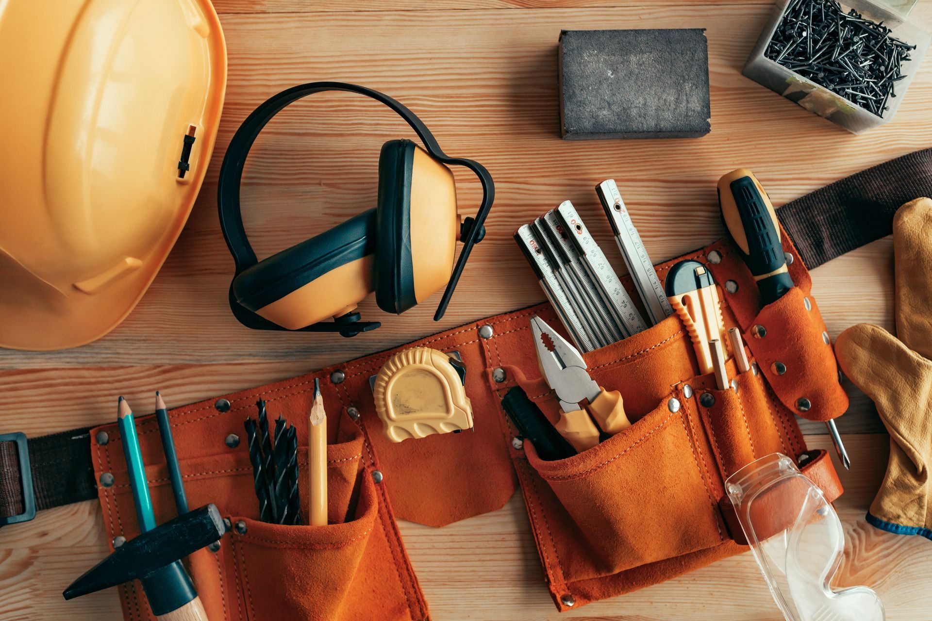 Tool belt with hand tools and construction equipment arranged on a wooden workbench.