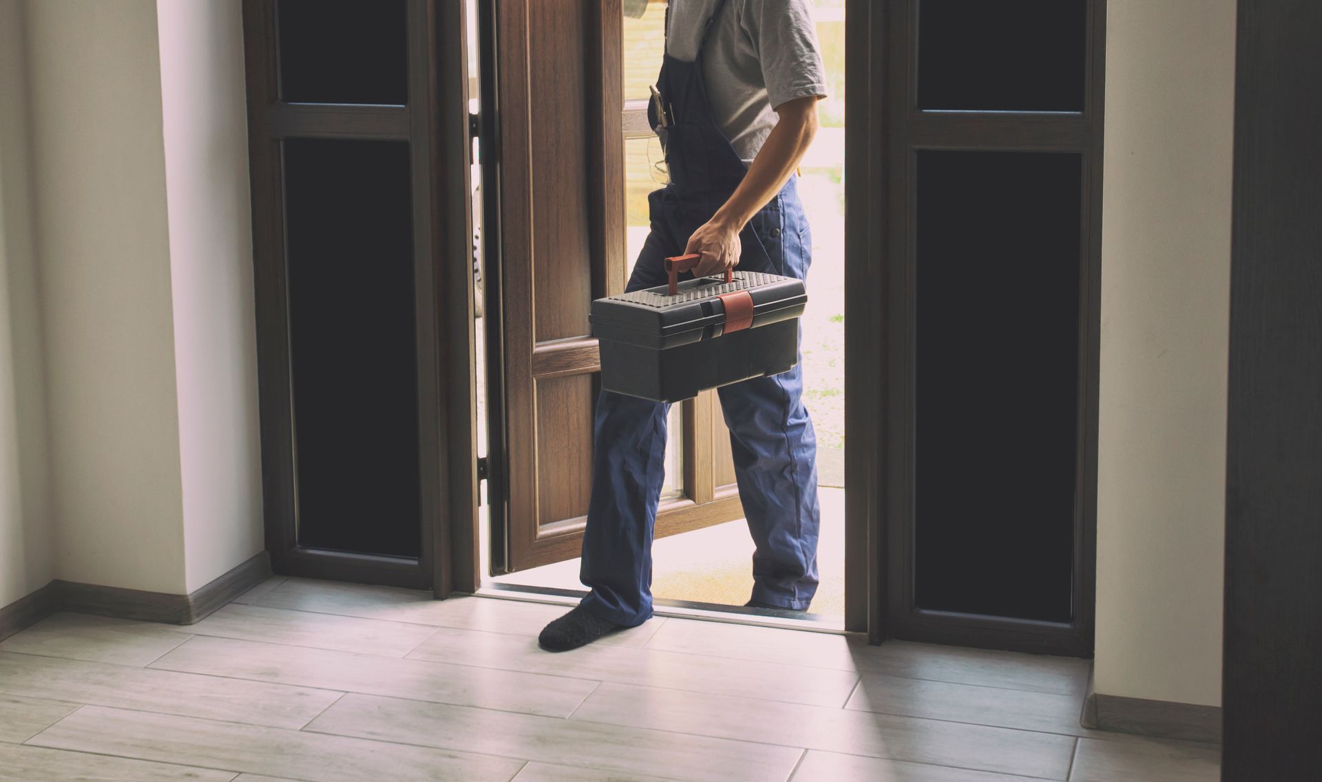 Person carrying a basket steps through a doorway into a dim hallway.