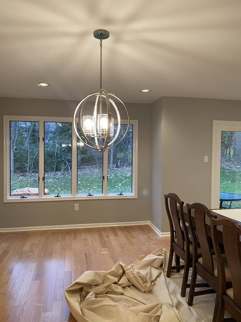 Modern dining room with hardwood floors, a hanging globe light, and large windows overlooking trees.