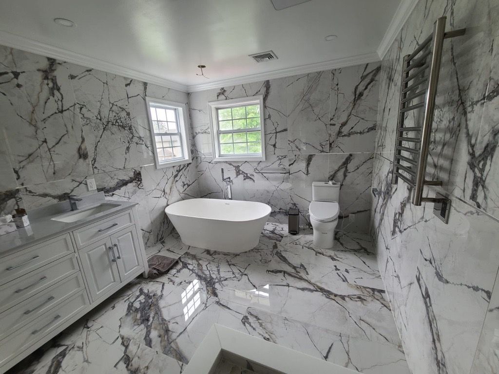 Luxury bathroom with white marble walls and floors, freestanding tub, toilet, vanity, and ladder towel rack.