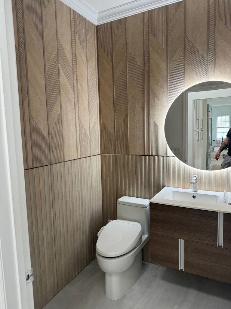 Modern bathroom with wood-paneled walls, toilet, sink vanity, and round mirror.