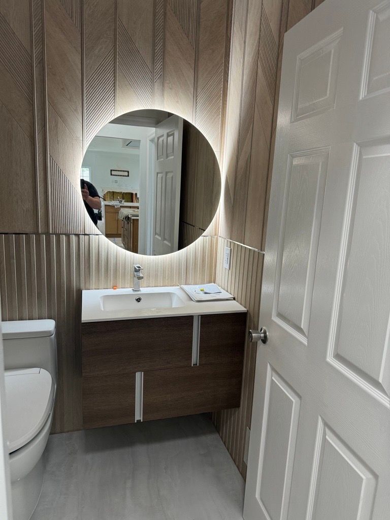 Small bathroom with wood-pattern walls, round mirror, white sink, and open door.