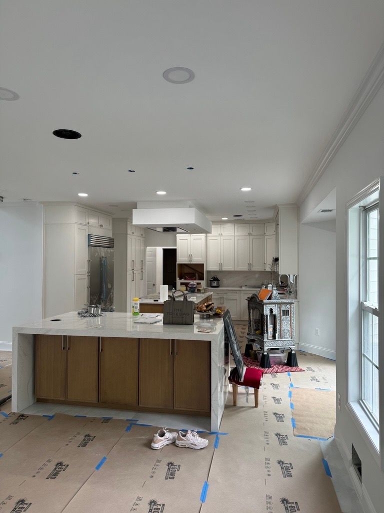 Bright kitchen under renovation with island, white cabinets, and protective floor covering