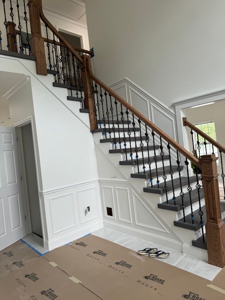 Interior staircase with wooden handrails, black balusters, and white walls in a foyer under renovation.