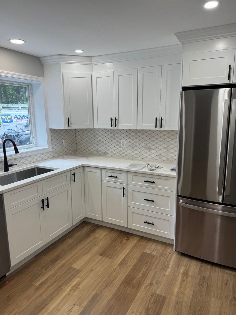 Bright white kitchen with stainless steel fridge, white cabinets, marble backsplash, and wood floor