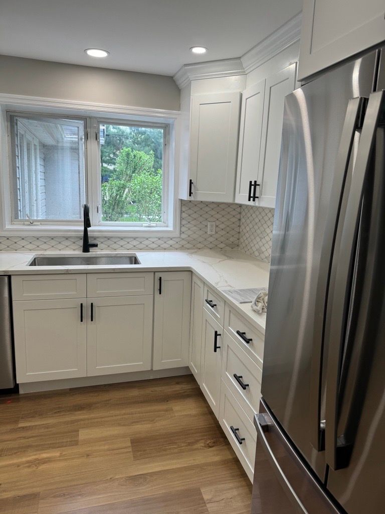 Bright modern white kitchen with stainless steel fridge, window over sink, and wood floor