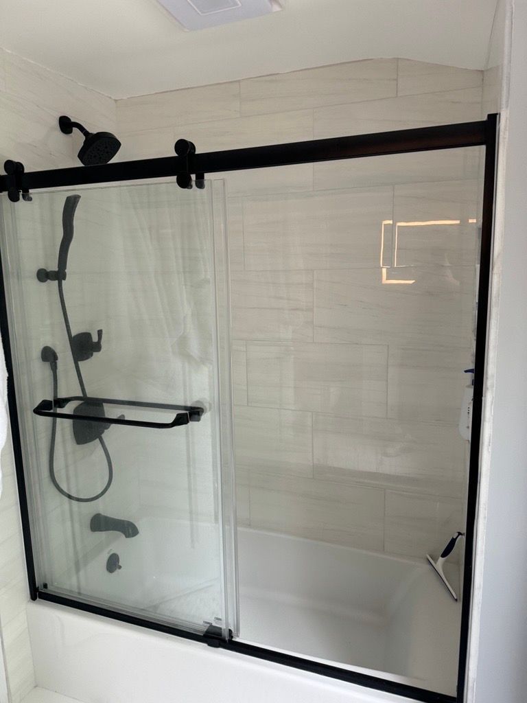 Black-framed glass shower enclosure with white tile walls and a built-in shelf