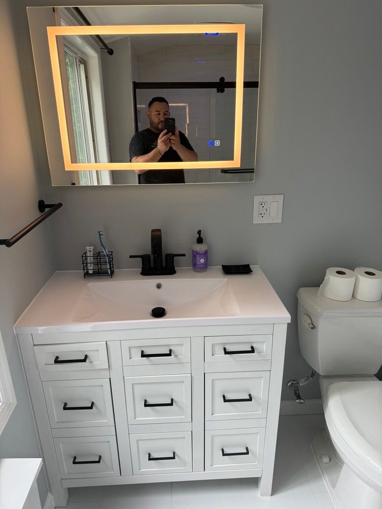 Bathroom vanity with illuminated mirror, white cabinet, toilet paper holder, and toiletries on the counter