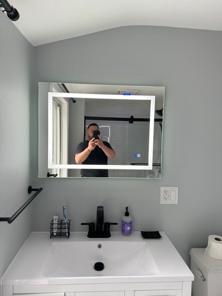 Bathroom vanity with white sink, mirror, gray wall, and toiletries on the counter.