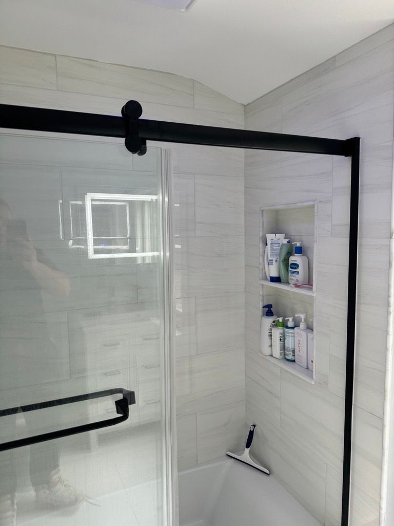 Modern tiled shower with glass door and built-in niche holding toiletries