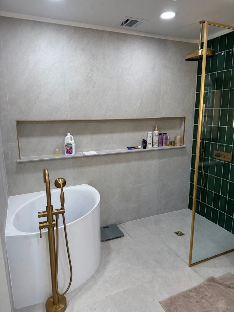 Modern bathroom with a freestanding tub, brass fixtures, and a glass shower with green tile accents