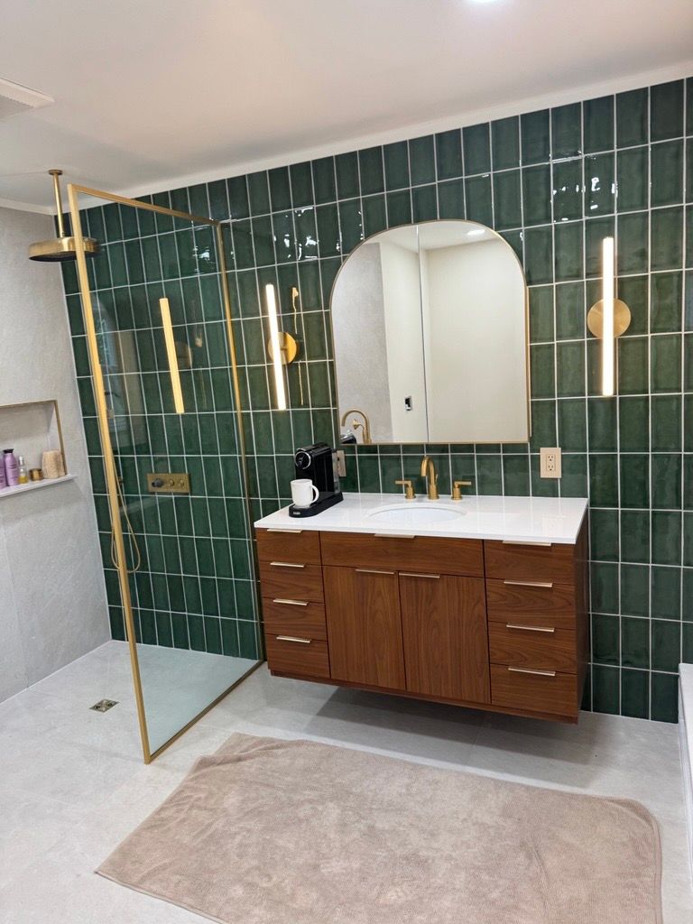 Modern bathroom vanity with green tile wall, wood cabinet, mirror, and beige rug