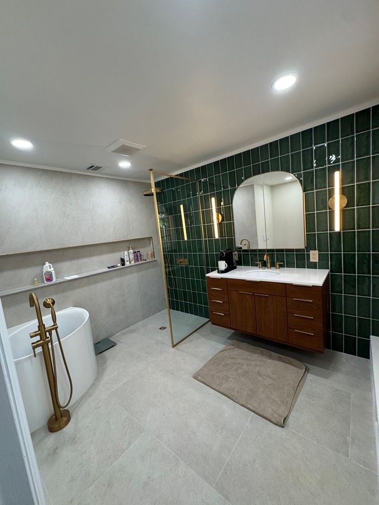 Modern bathroom with green tile wall, wood vanity, gold fixtures, and glass shower partition