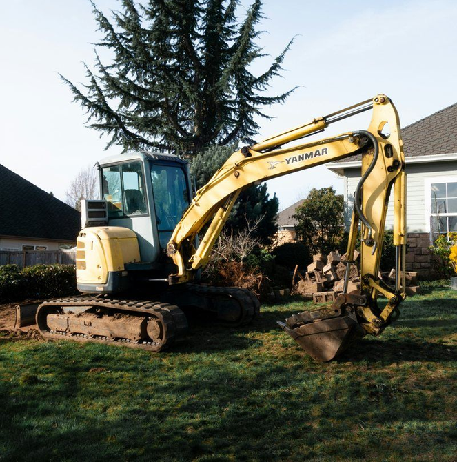 Mini excavator positioned in a residential yard before drainage work