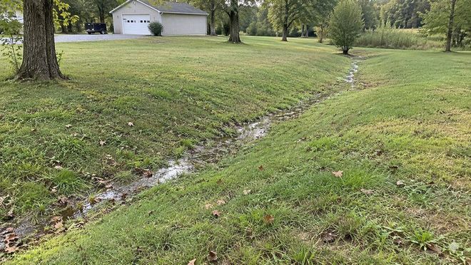 Shallow grass drainage channel carrying water through a lawn