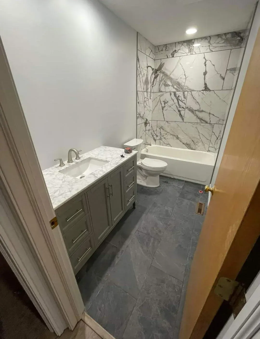 Small modern bathroom with marble vanity, gray floor, and marble shower wall.