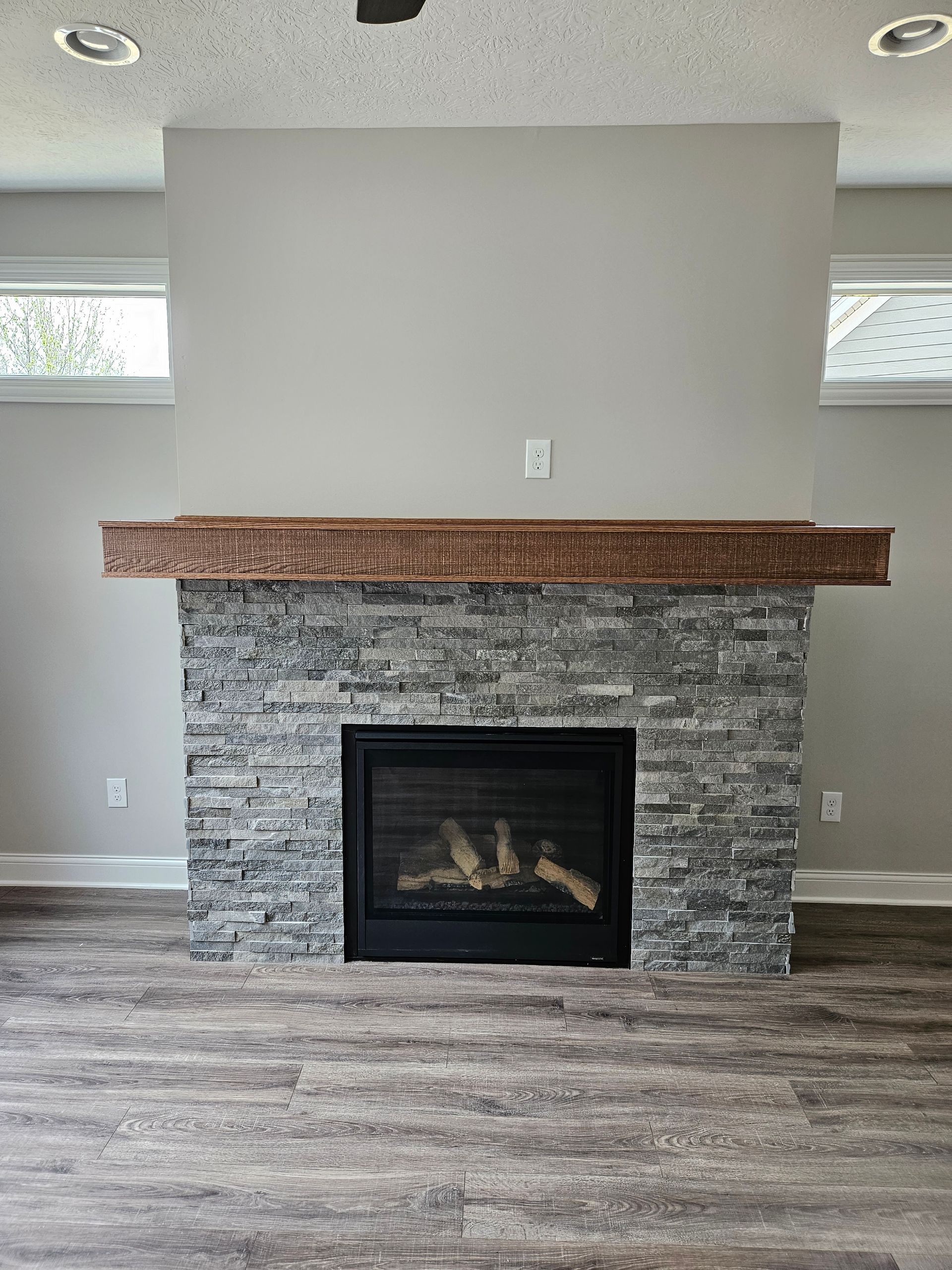 Living room fireplace with gray stone surround, wood mantel, and wood-look flooring