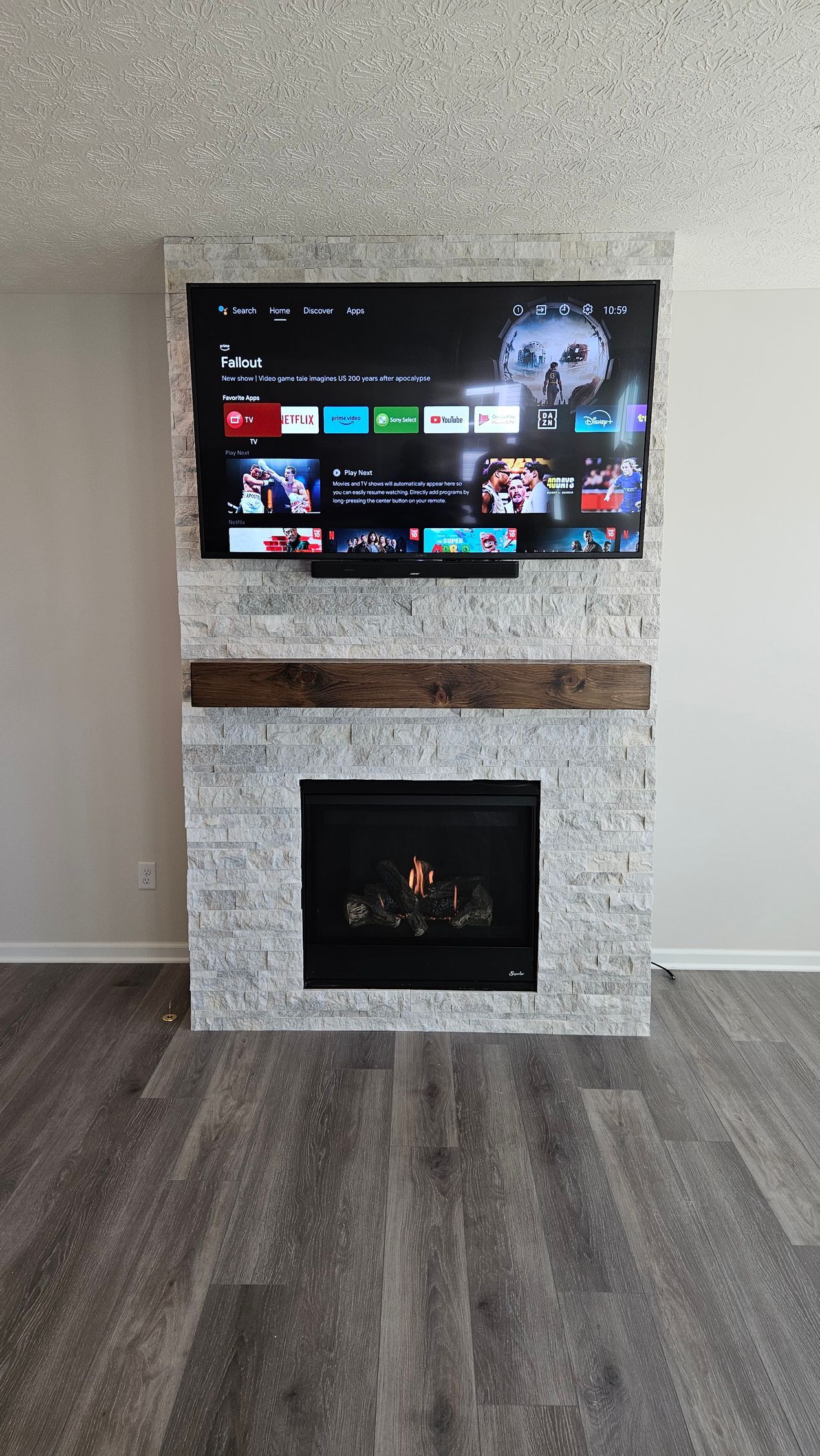 Modern fireplace with a mounted TV above it in a minimalist living room with gray wood flooring.