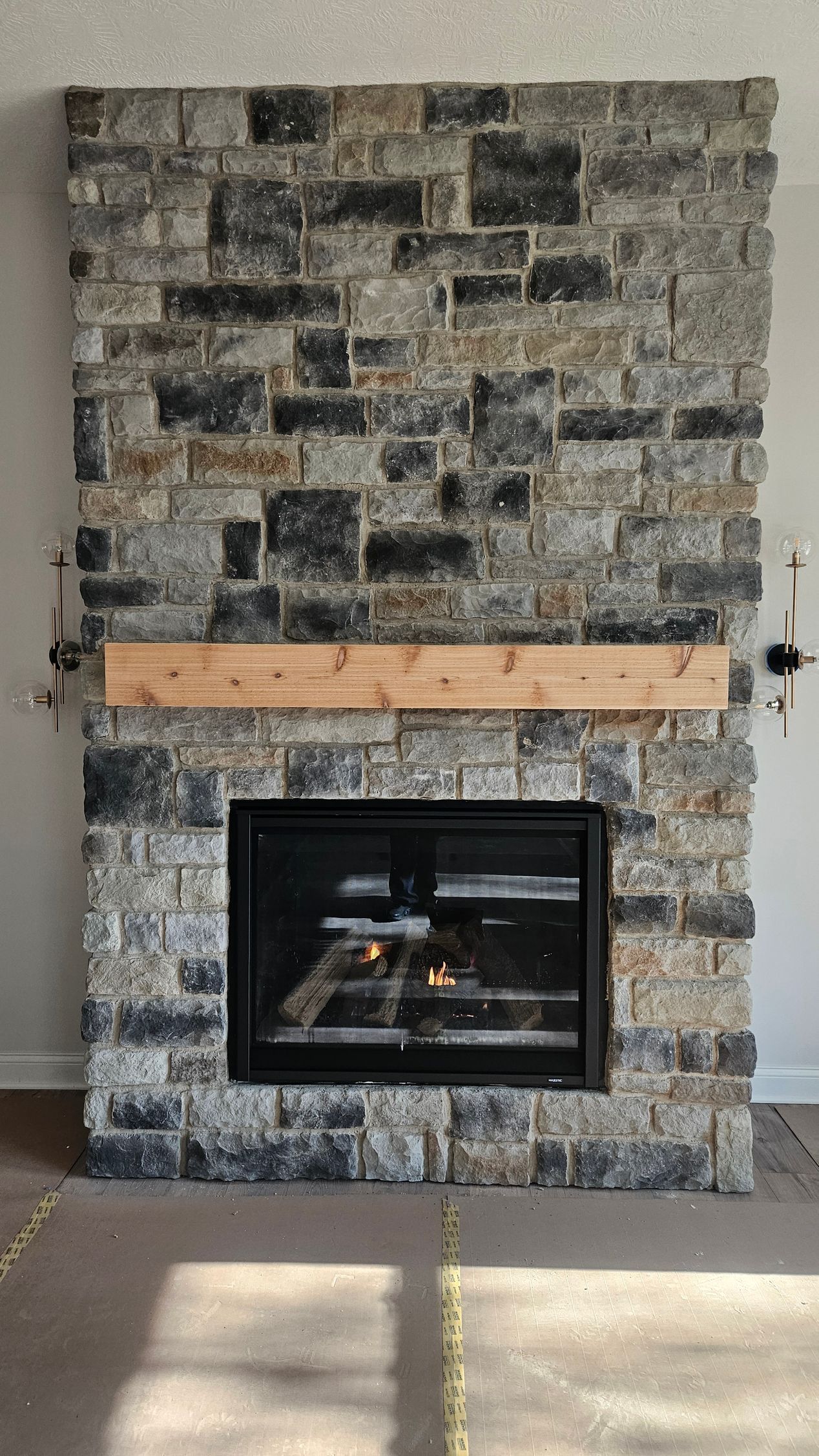 Stone fireplace with black gas insert and light wood mantel in a living room