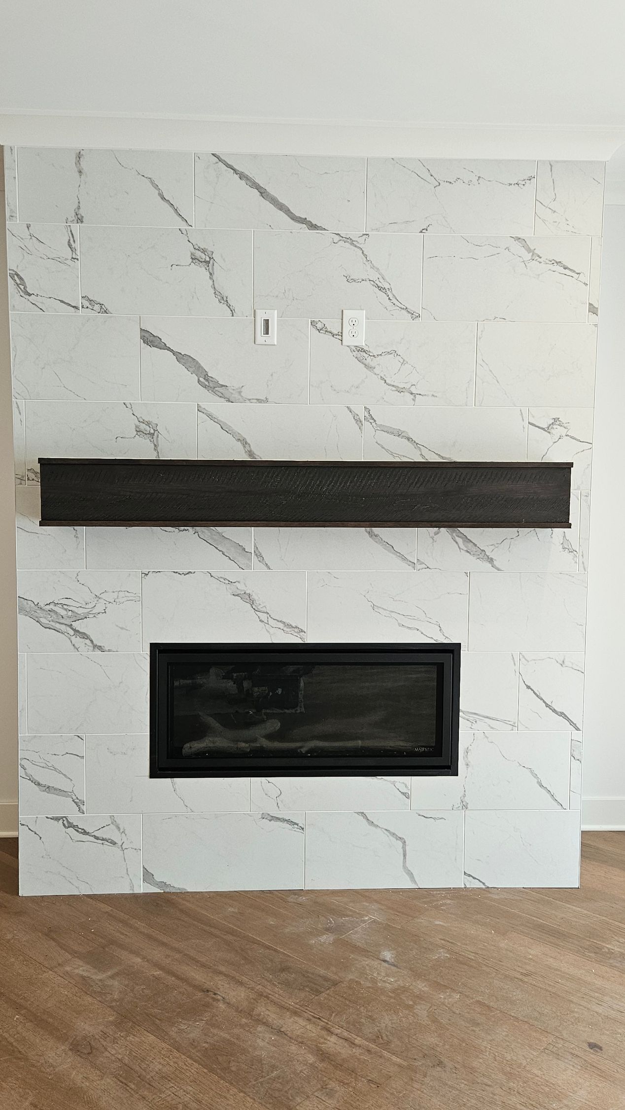 White marble fireplace with a black mantel and recessed black firebox against a wood floor.