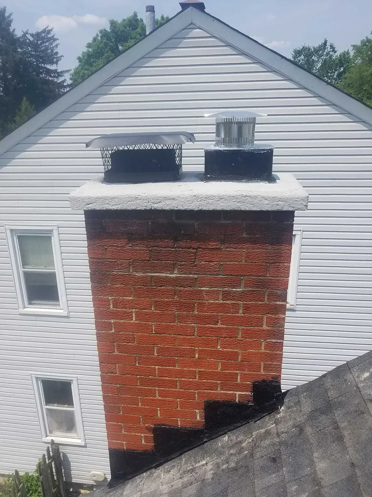 White house exterior with a large red brick chimney and two small upper windows on a sloped roof