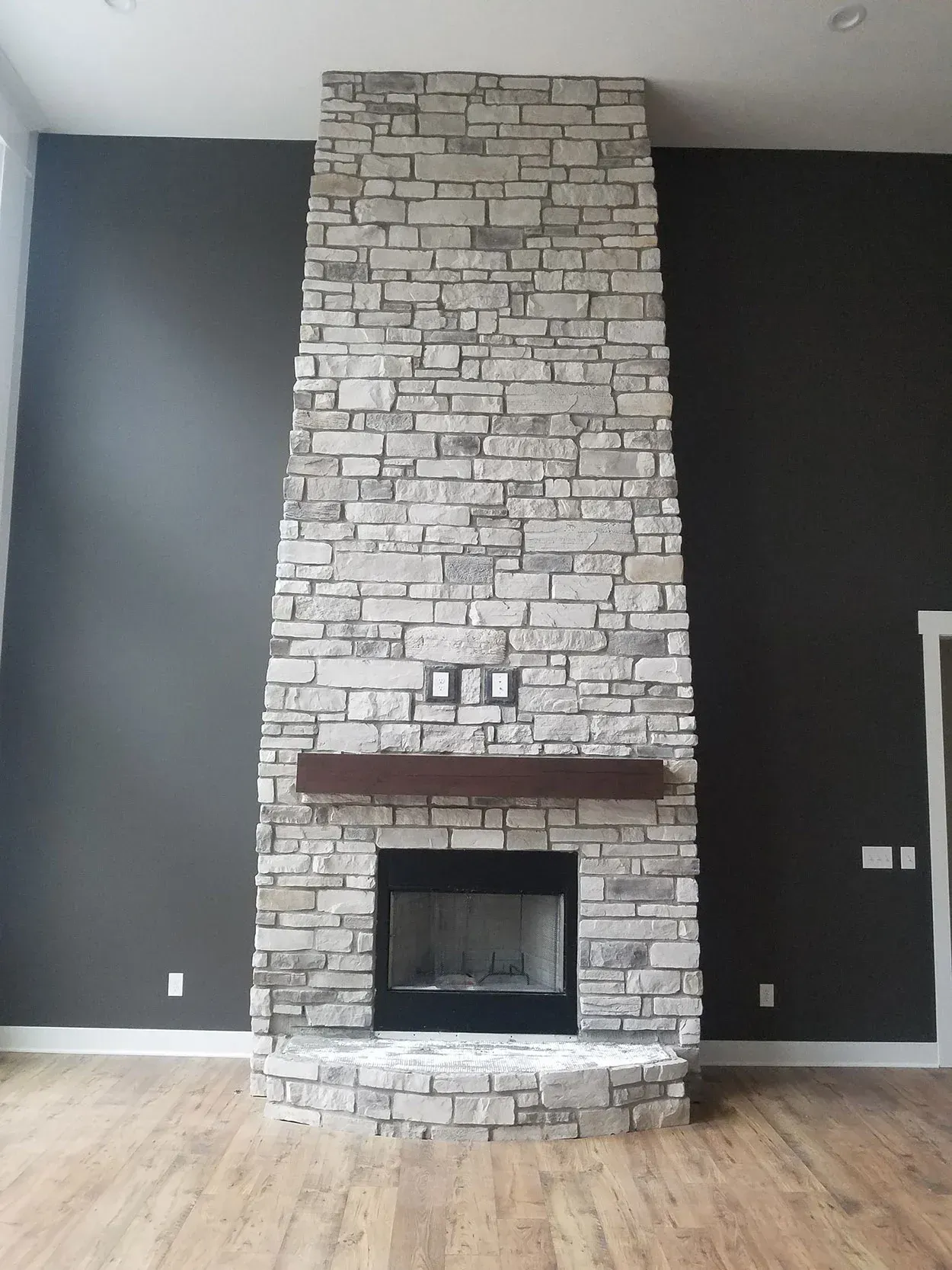 Living room with a stone fireplace and dark gray walls on hardwood floors