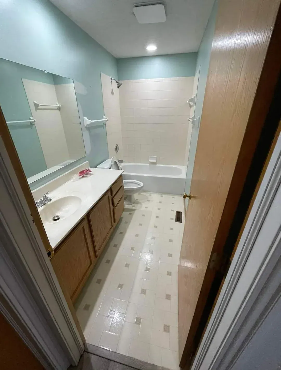 Narrow bathroom with white tub, sink vanity, mirror, and light blue walls viewed through a doorway