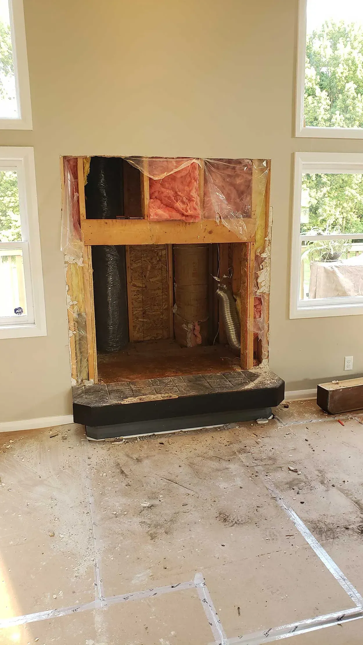 Partially demolished fireplace wall in a room with windows and debris on the floor