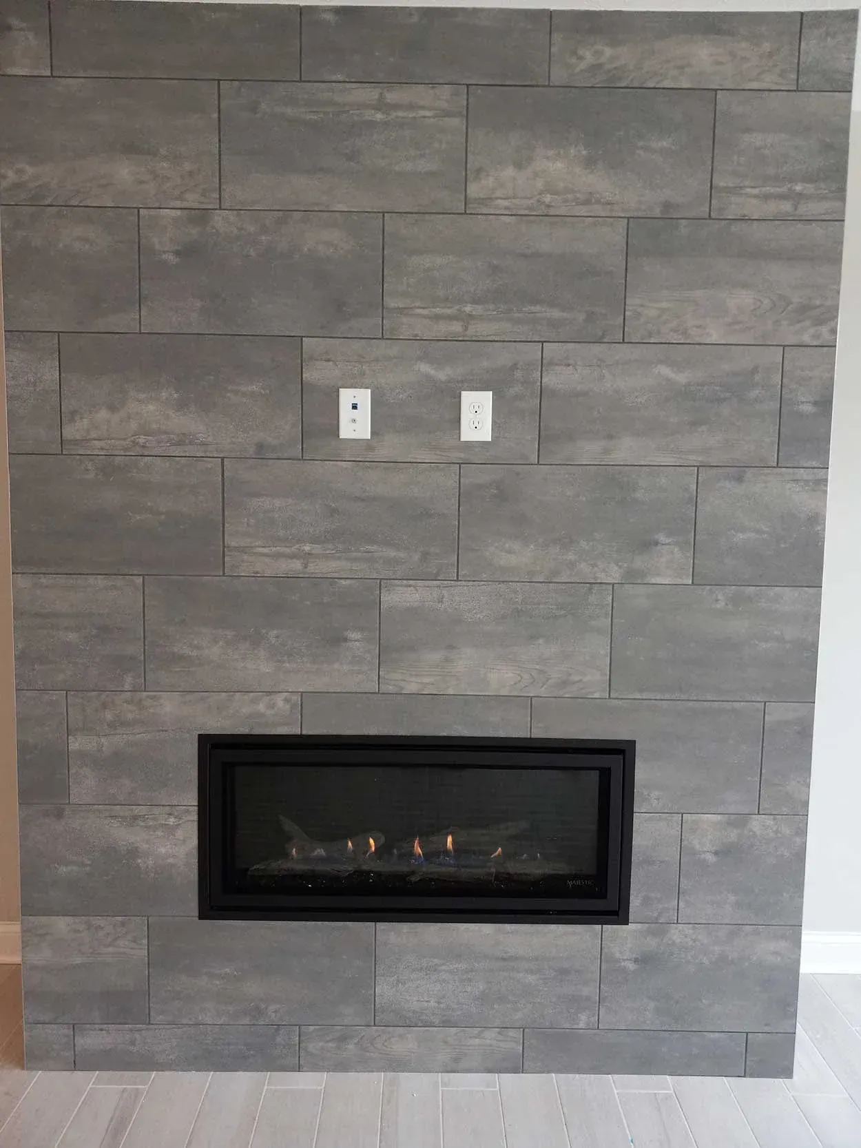 Gray stone fireplace wall with a black electric fireplace insert and two wall outlets above it.