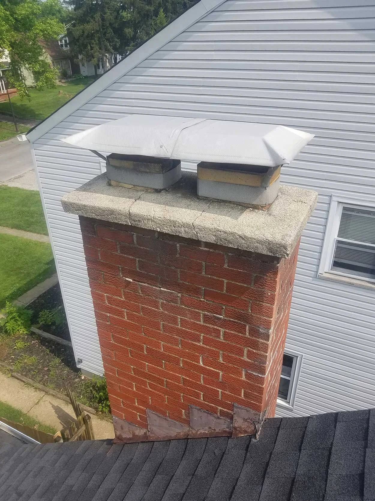 Brick chimney with two vents on a gray shingled house roof