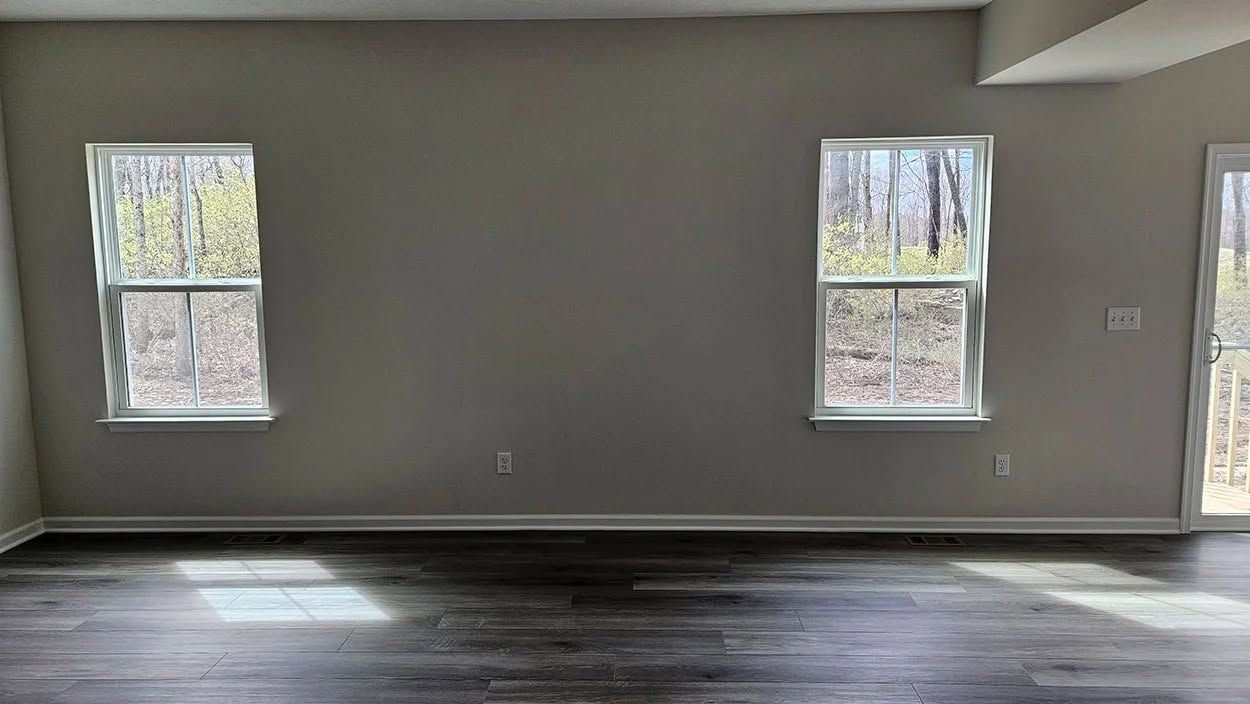 Empty living room with gray walls, dark wood floors, and two windows letting in daylight