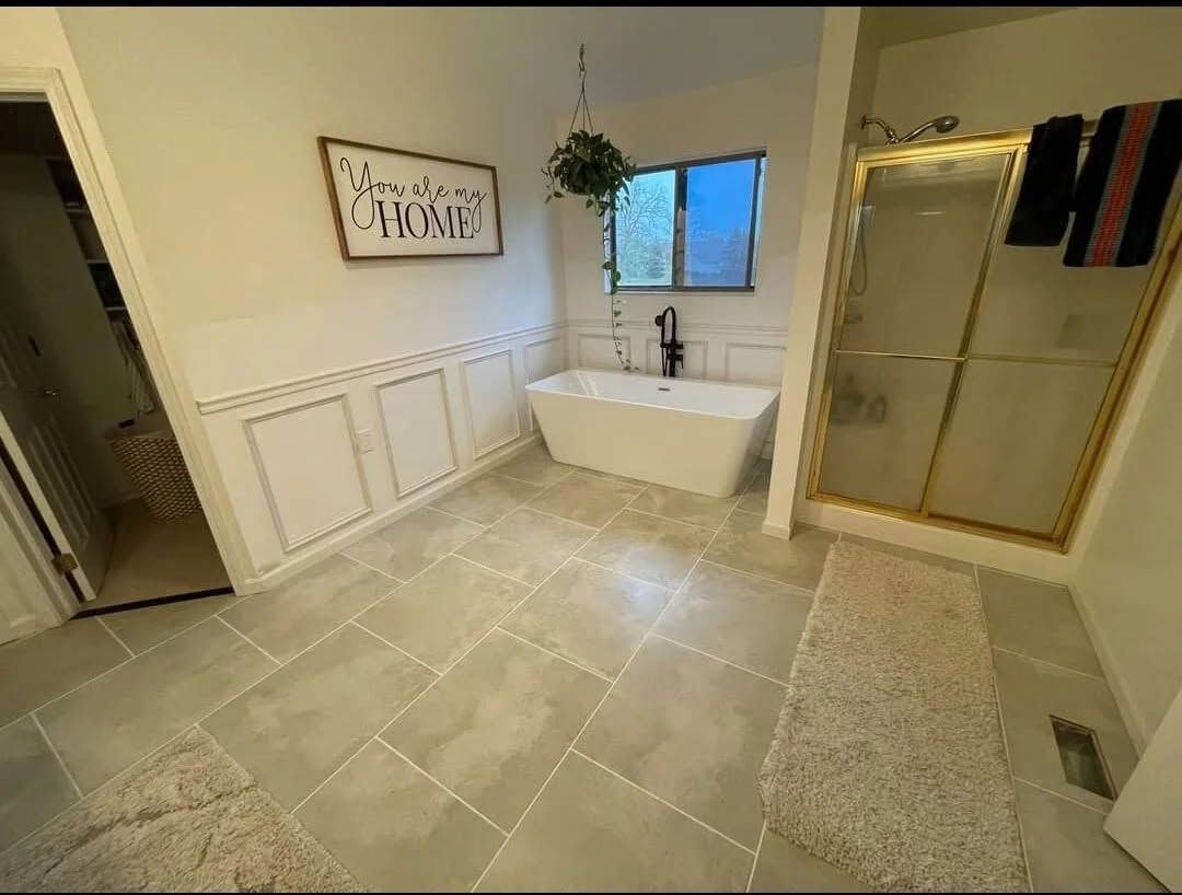 Spacious tiled bathroom with a soaking tub, glass shower, window, and wall art.