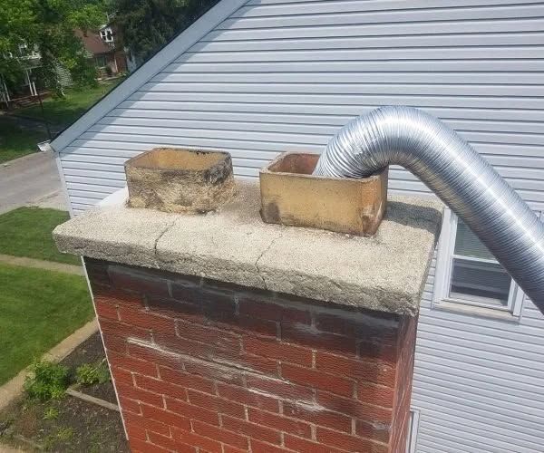 Brick chimney with two metal vent caps and a silver flex duct on a house roof