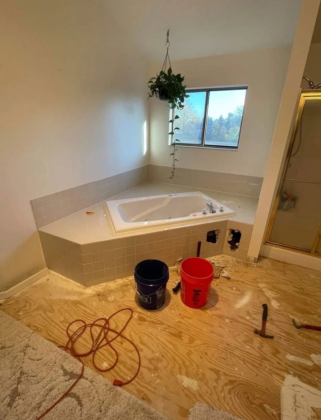 Bathroom under renovation with a built-in tub, tools, buckets, and exposed subflooring.