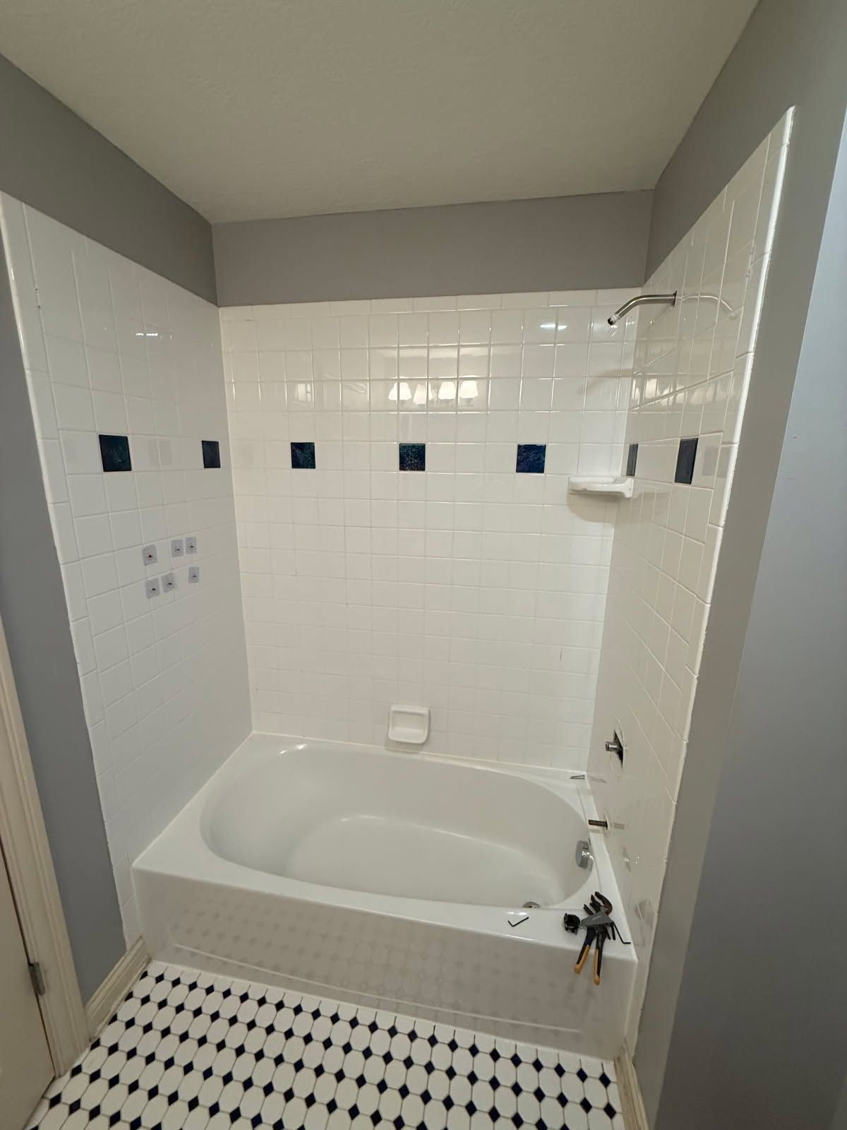 Small bathroom with white tiled bathtub, gray walls, and black-and-white checkered floor.