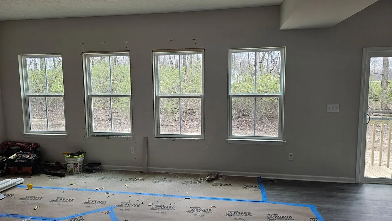 Empty living room under renovation with gray walls, taped floor protection, and five windows along one wall