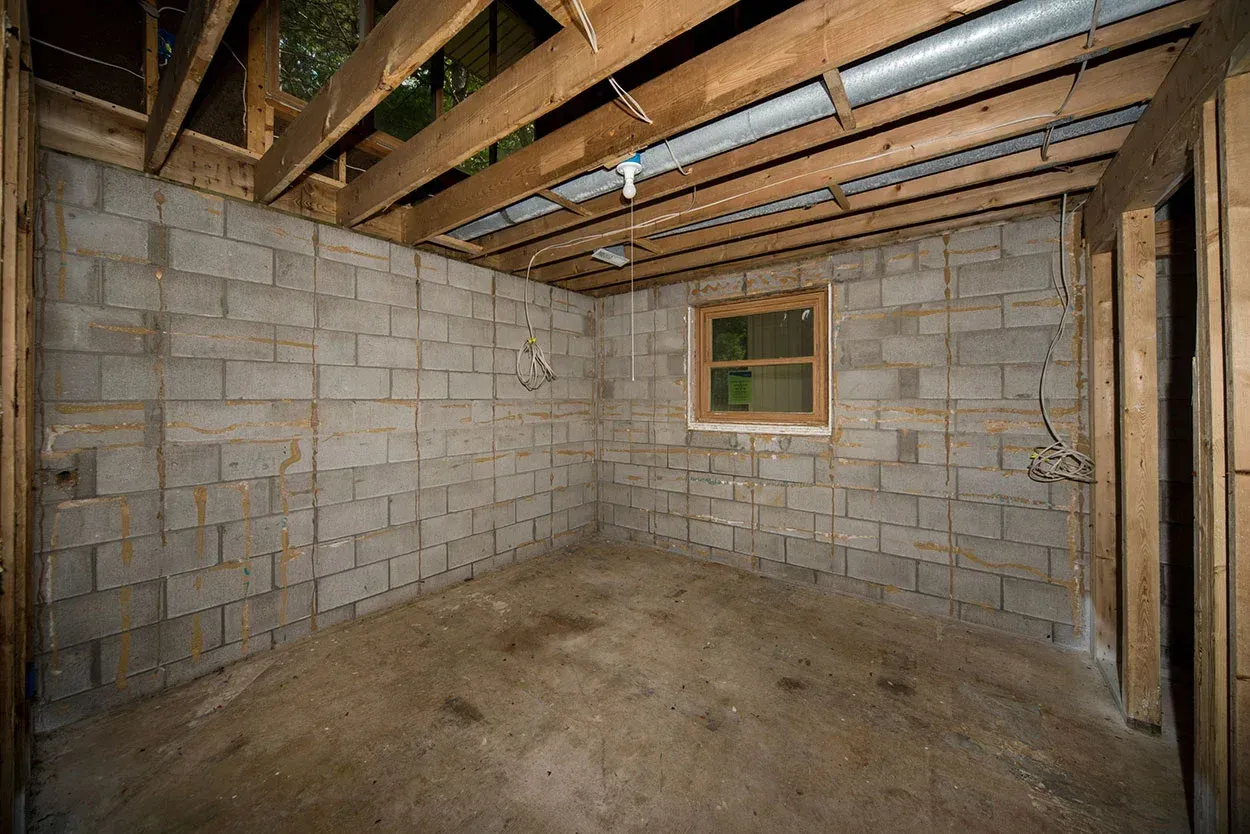 Unfinished basement with cinder block walls, exposed beams, and a small window.