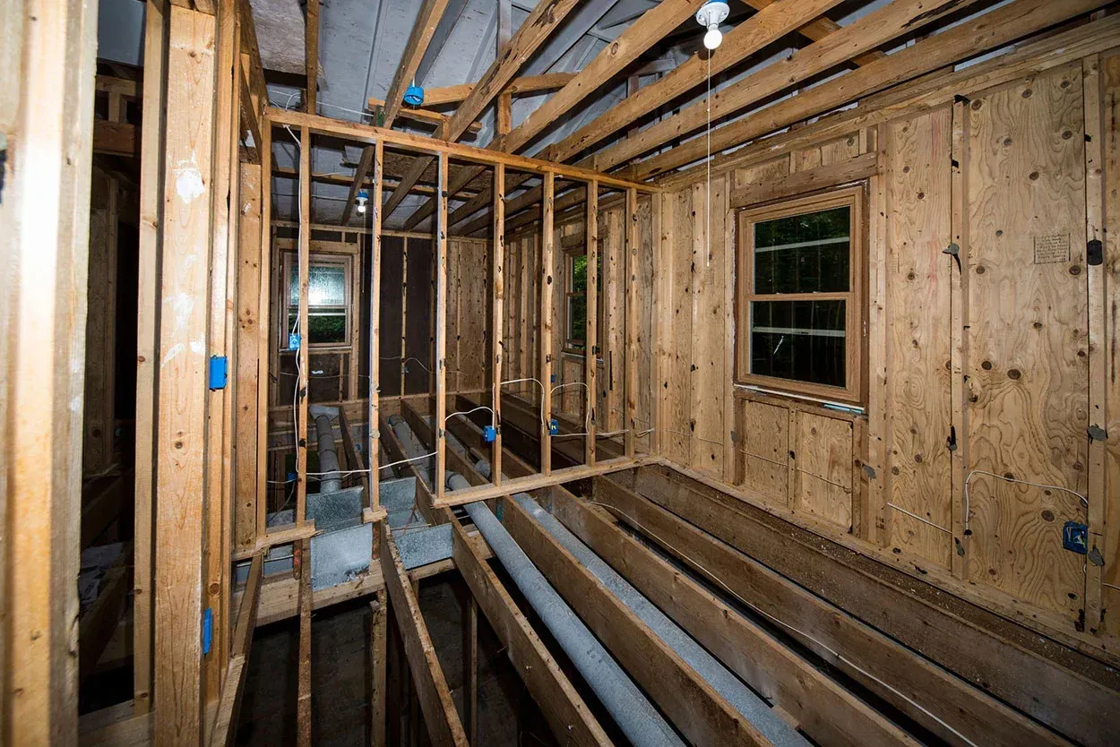 Unfinished room with exposed wooden framing, floor joists, and a window in a construction site.