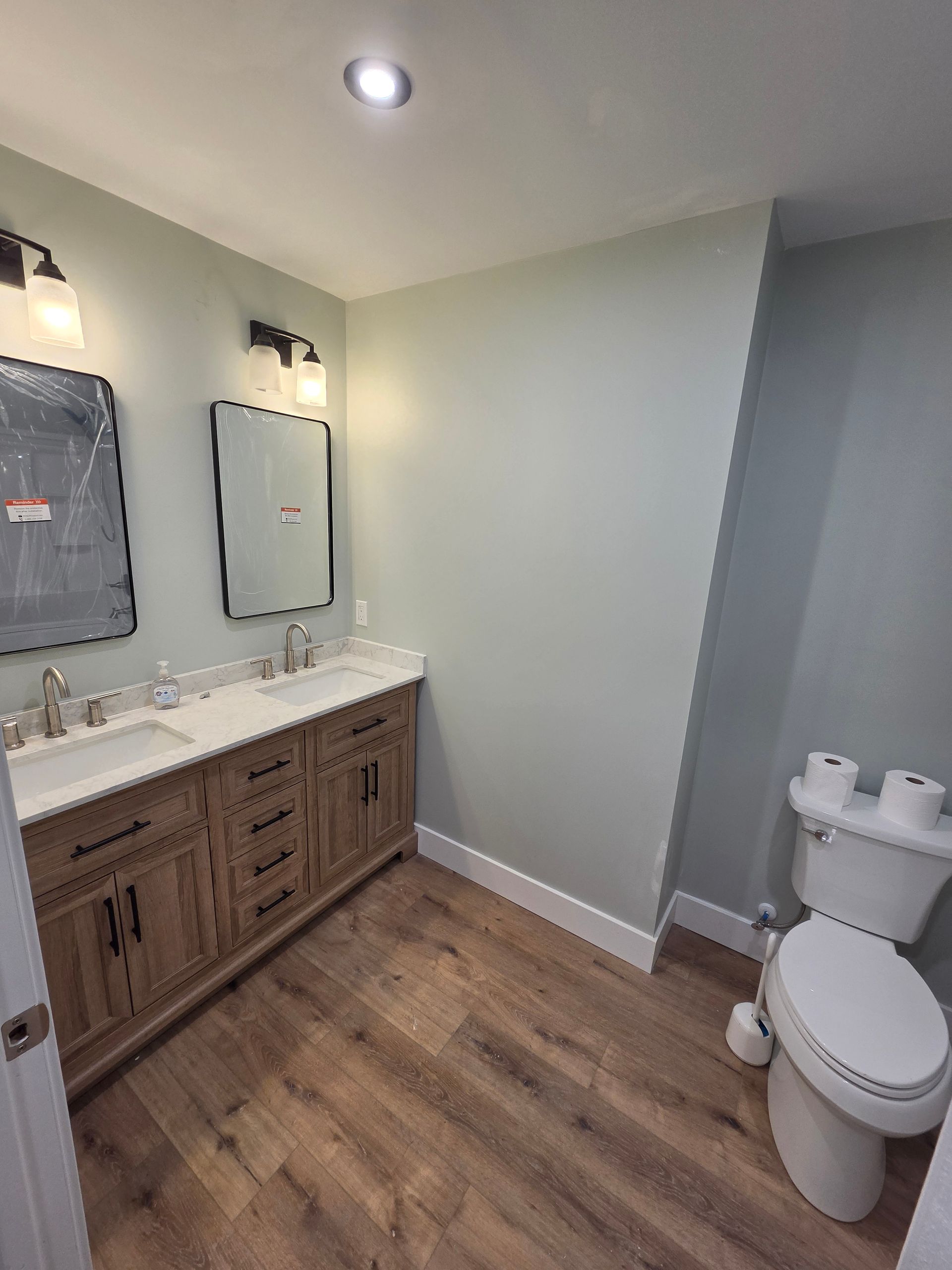 Modern bathroom with wood vanity, white sink, mirror, toilet, and wood-look floor
