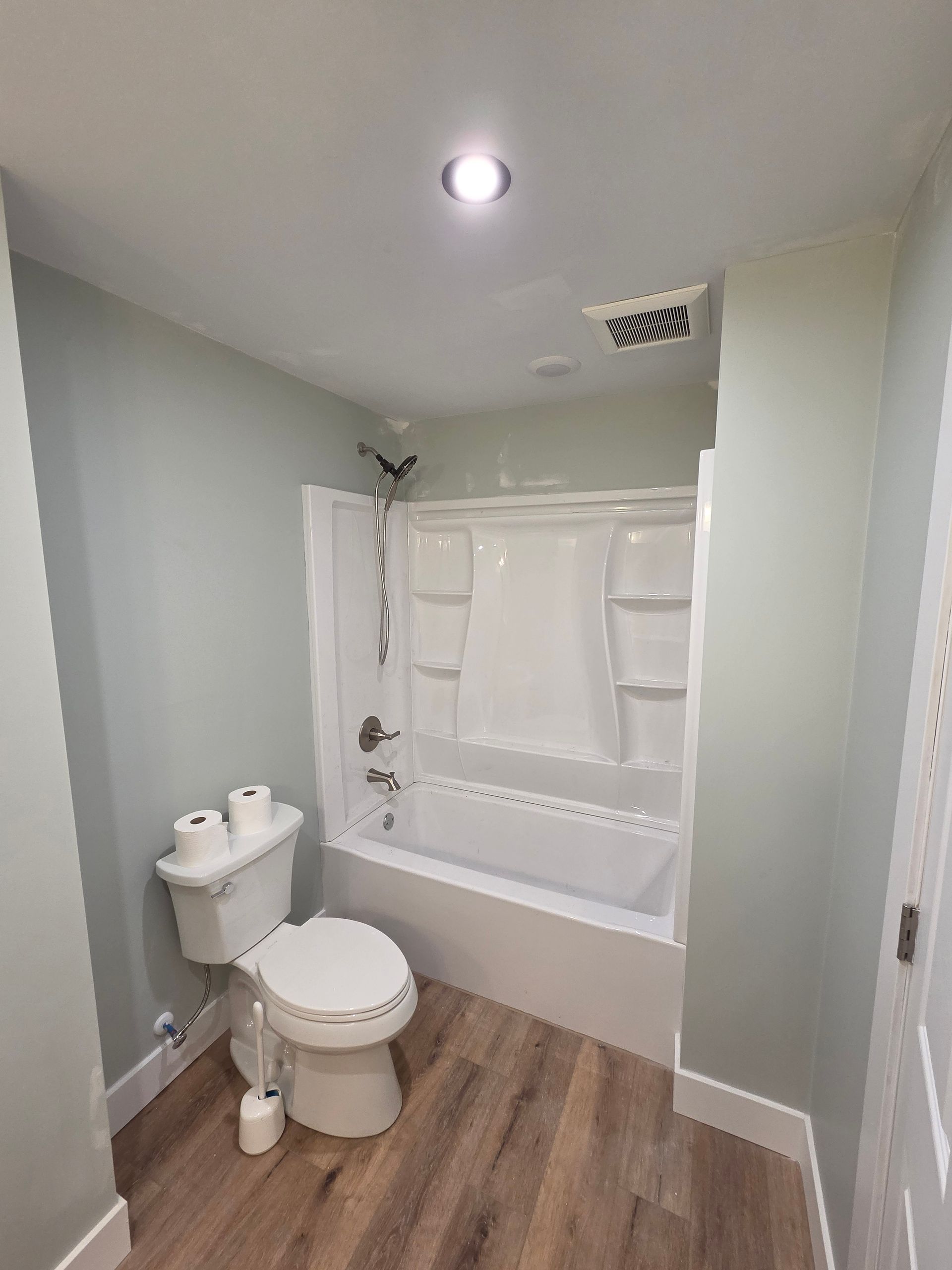 Small bathroom with toilet, sink, tub-shower, and wood-look flooring under bright ceiling light