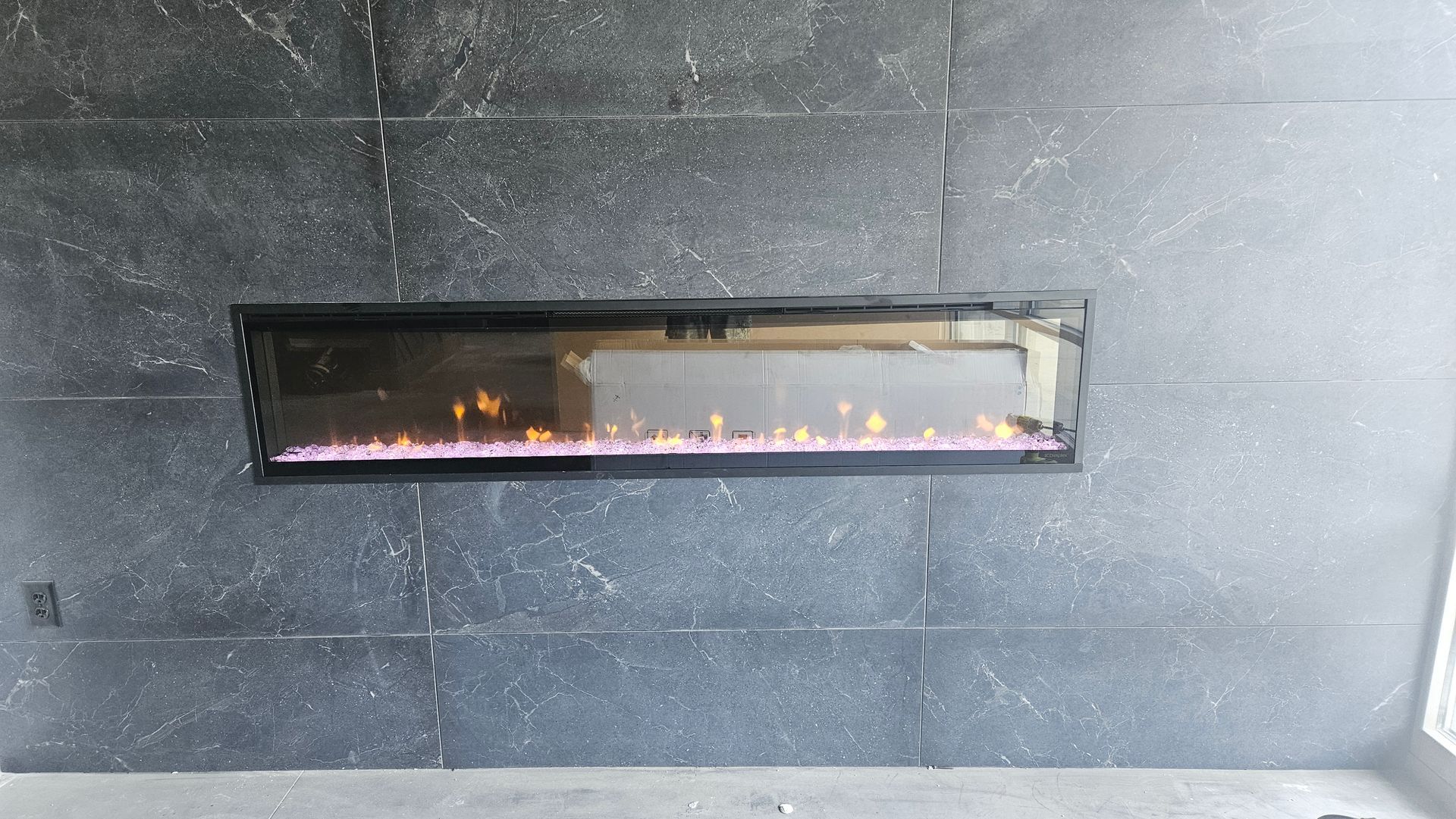 Modern wall-mounted electric fireplace with orange flames set in a dark stone wall interior