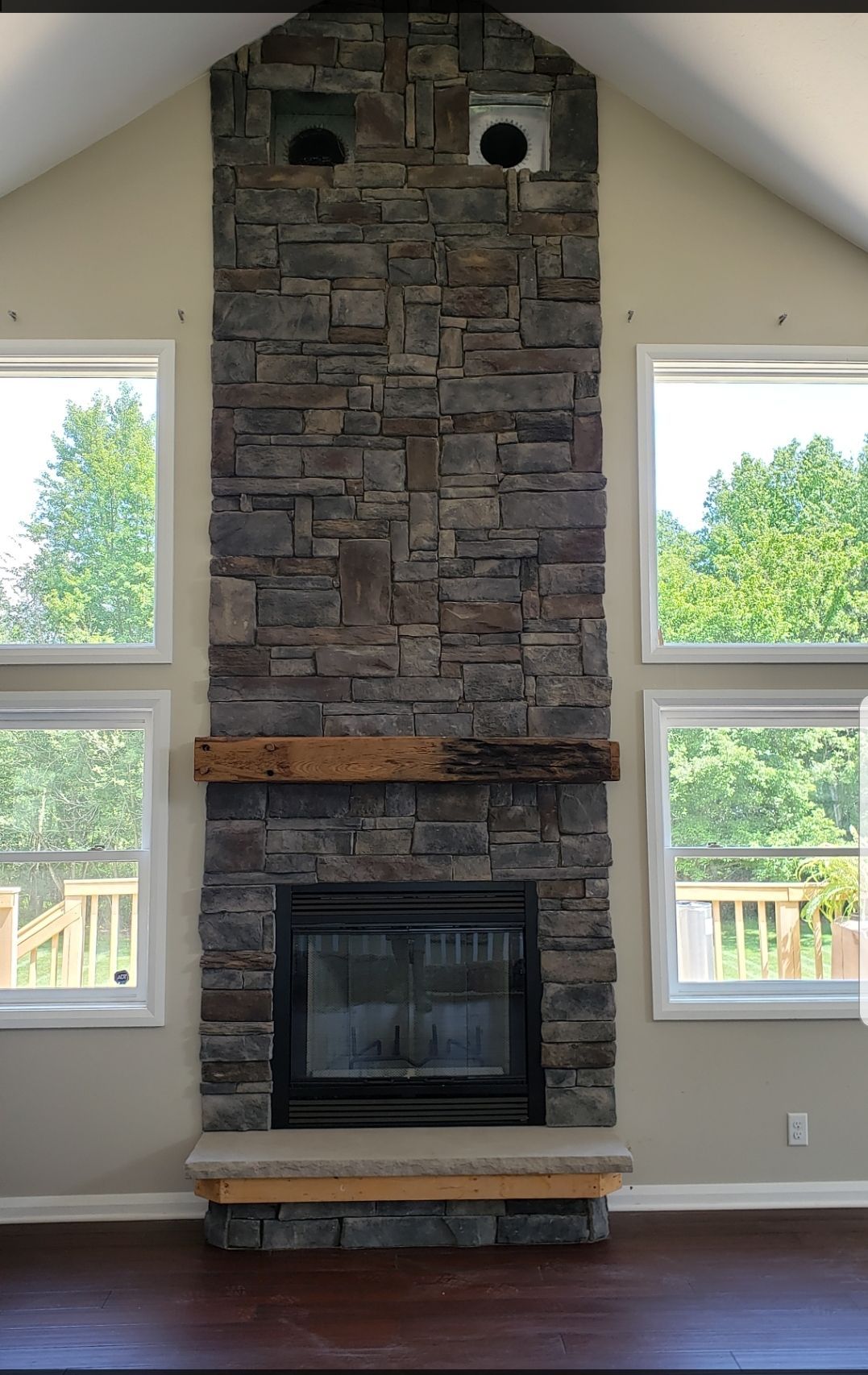 Stone fireplace centered between two windows in a bright room, with a wooden mantel and hearth.